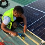 Technician working on solar panel installation with cables and tools on a sunny day.